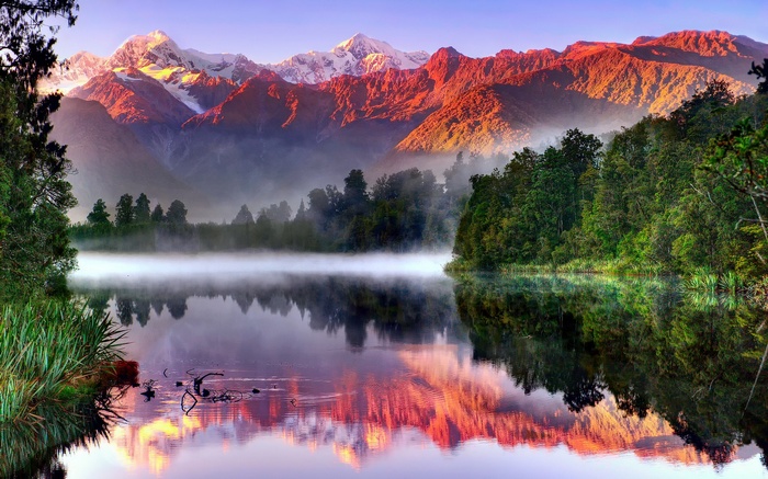 Misty lake reflecting snow-capped mountains at sunrise