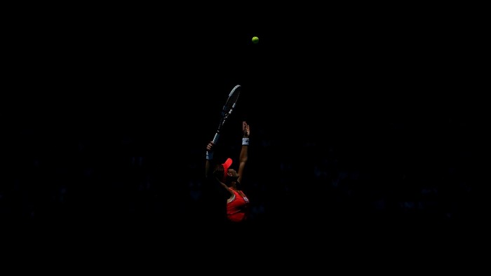 Tennis player serving in darkness