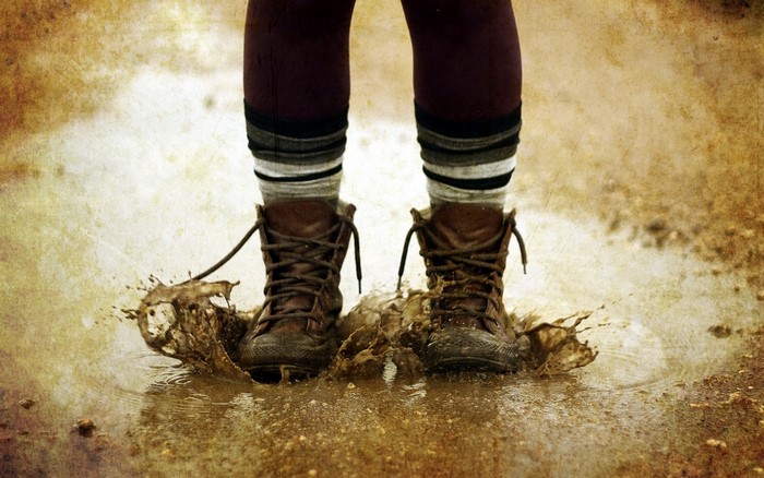 Person jumping in muddy puddle wearing boots