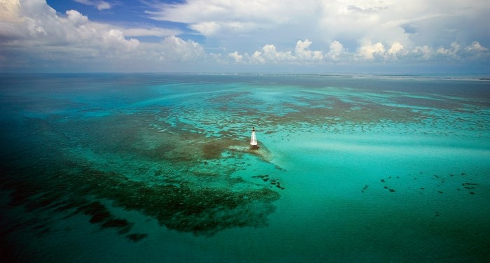 Lighthouse in turquoise water with coral reef and clouds