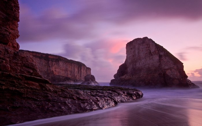 Purple sunset over rocky coast with ocean waves