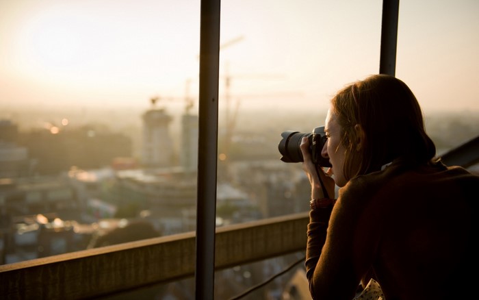 Woman photographing city skyline at sunset
