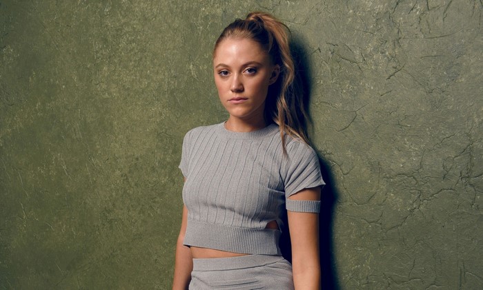 Maika Monroe leaning against a textured green wall