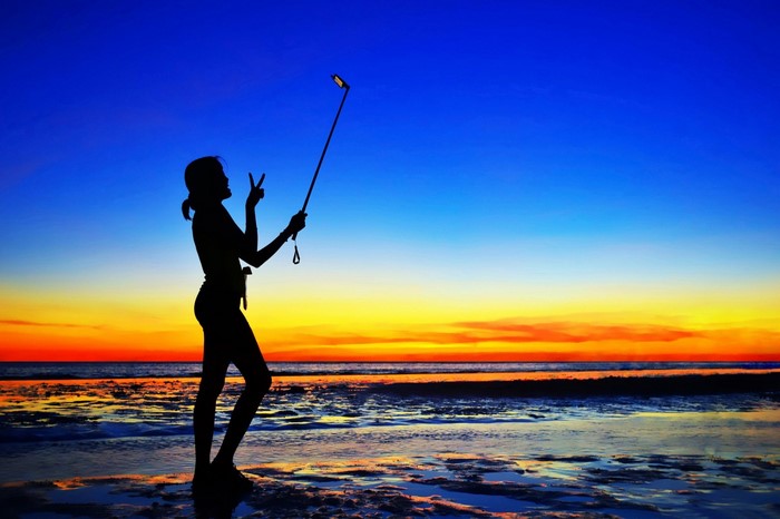 Silhouette of a woman taking a selfie at sunset on a beach
