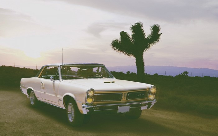 White Pontiac GTO parked in a desert landscape at sunset