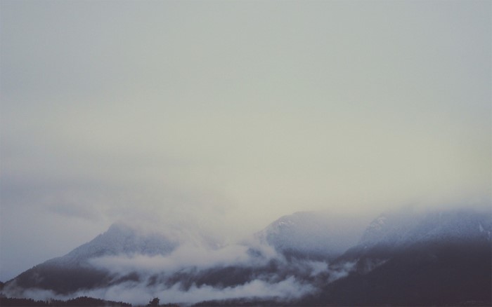 Misty mountains shrouded in fog under a pale sky