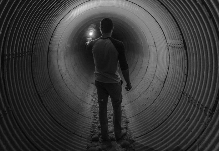 Man holding flashlight in a corrugated metal tunnel