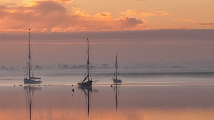 Sailboats on misty water at sunrise or sunset