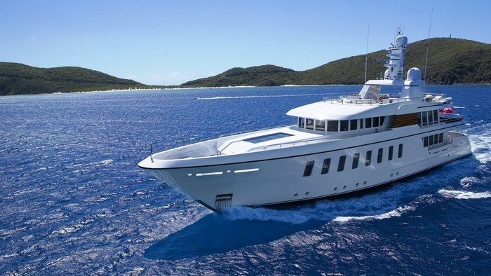 White luxury yacht sailing on blue ocean near green islands