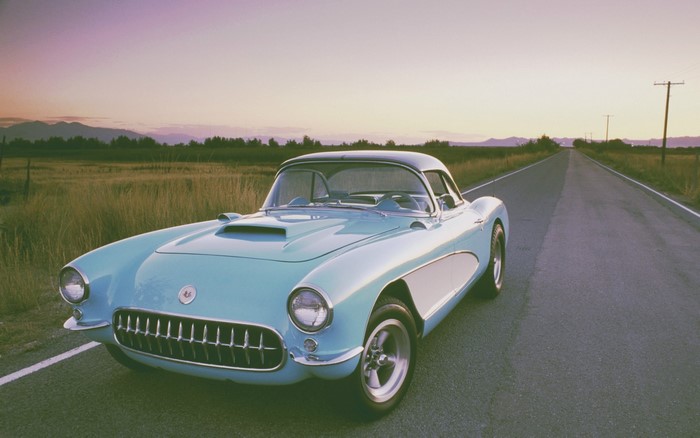 Vintage light blue Chevrolet Corvette on a rural road at sunset