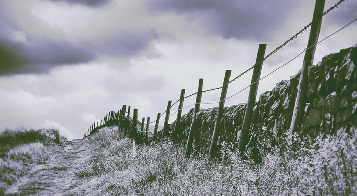 Stone wall and fence in a grassy field under cloudy sky