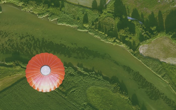 Red hot air balloon over green fields and river
