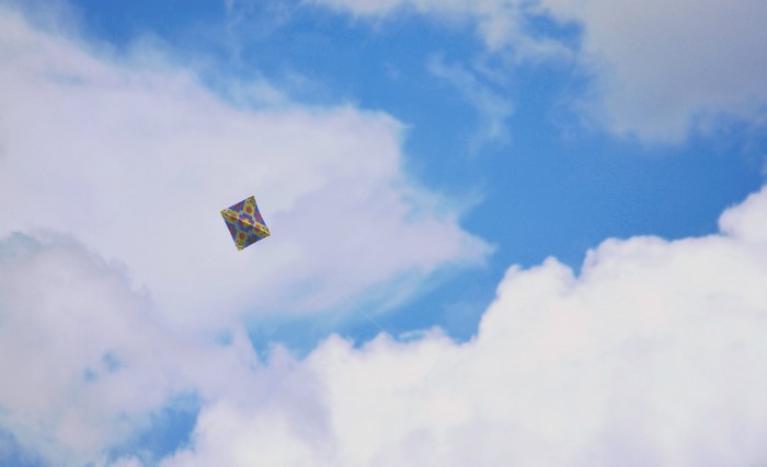 A colorful kite flying in a cloudy blue sky