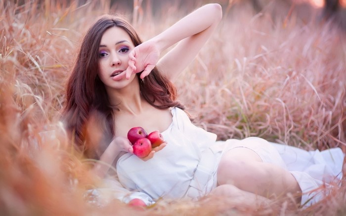 Woman in white dress holding apples in tall grass
