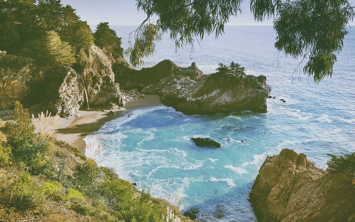 Waterfall cascading into a turquoise cove on a rocky coastline