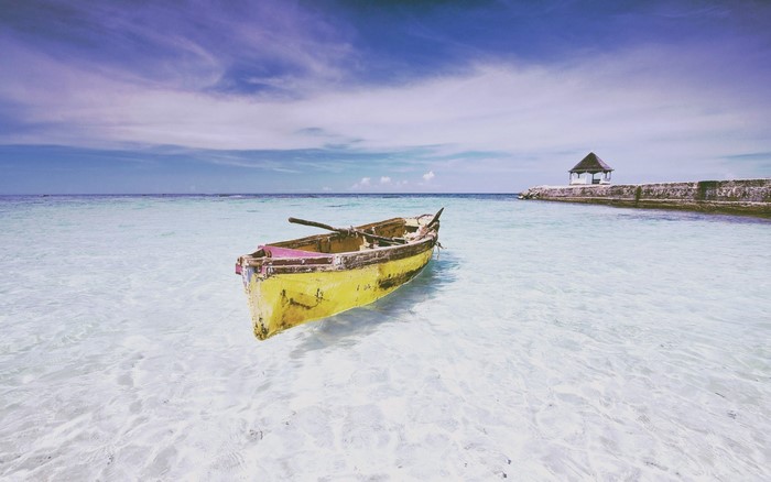 Yellow rowboat floating in clear turquoise water near a stone pier with a gazebo