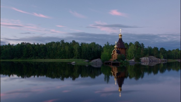 Wooden church with golden domes reflected in a calm lake at dusk