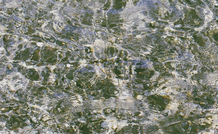 Water surface with pebbles and light reflections