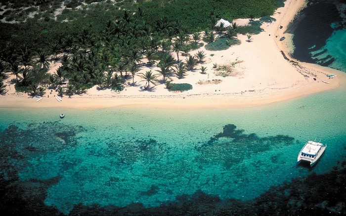 Aerial view of a tropical island beach with palm trees and a yacht