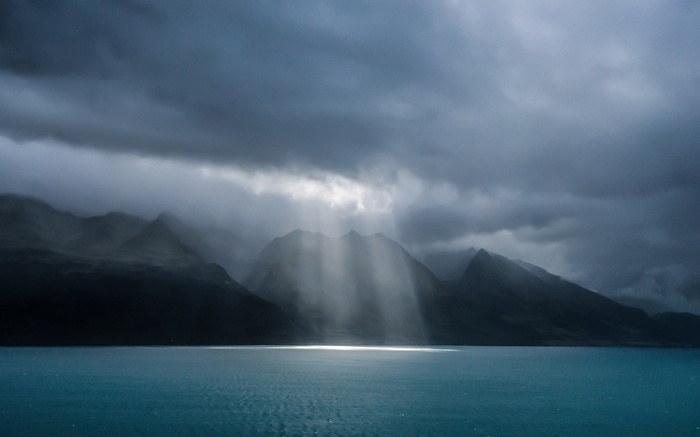 Sunbeams through clouds over mountains and water