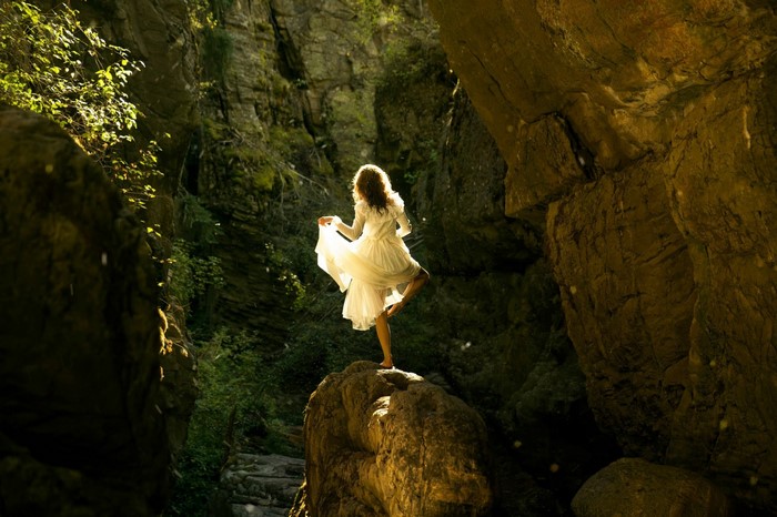 Woman in white dress dancing on a rock in a canyon