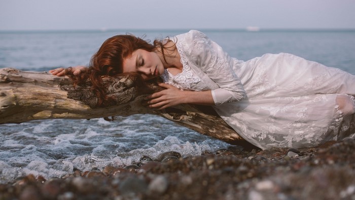 Woman with red hair sleeping on a log by the sea