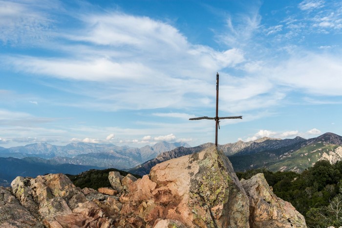Cross on a rocky mountain summit with distant mountain ranges