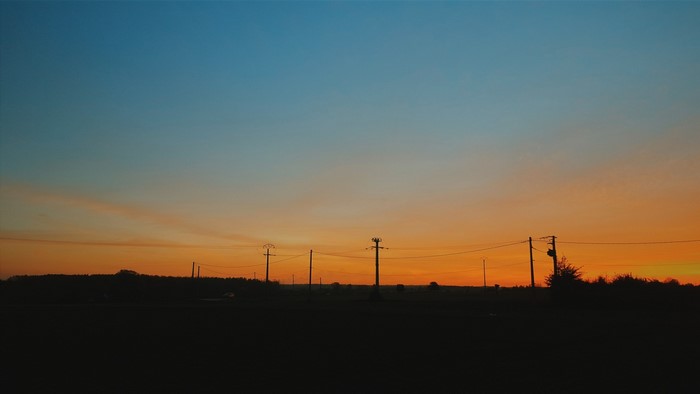 Silhouette of telephone poles against a sunset sky