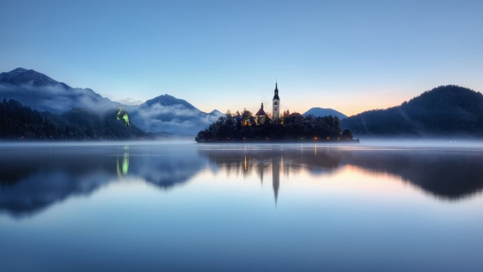 Island church in lake at dawn with misty mountains