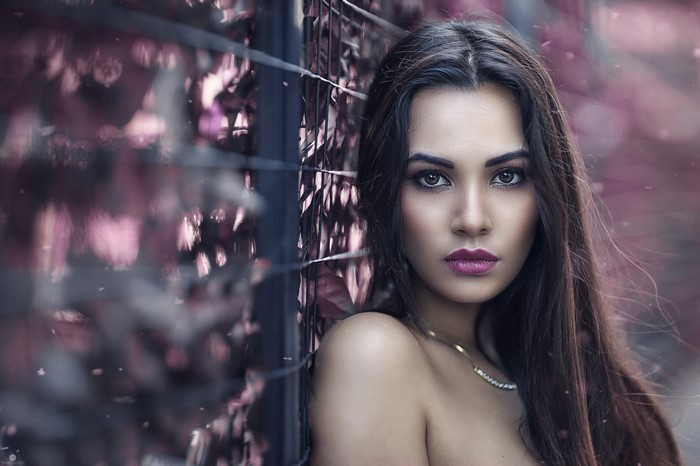 Woman leaning against a fence with pink foliage