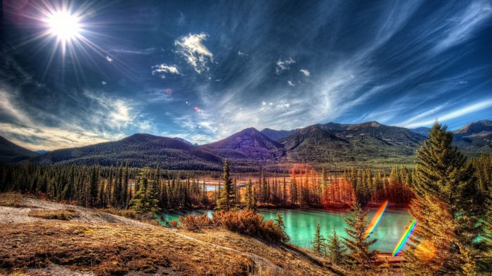 Sunlight over a mountain range and forest with a turquoise river