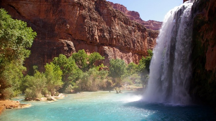 Waterfall cascading into a turquoise pool in a canyon