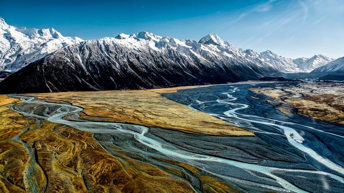 Aerial view of braided river flowing through a valley with snow-capped mountains