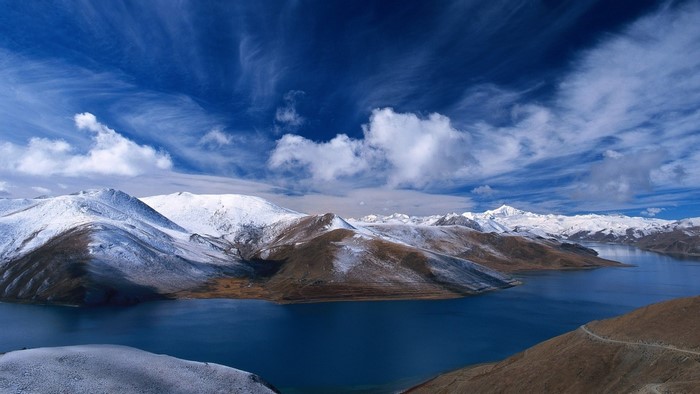 Snow-capped mountains surround a deep blue lake under a cloudy sky