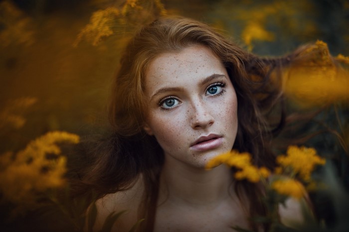 Young woman with freckles and blue eyes in yellow flowers