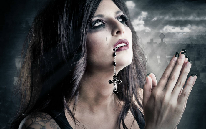 Gothic woman with rosary and cross praying in a graveyard