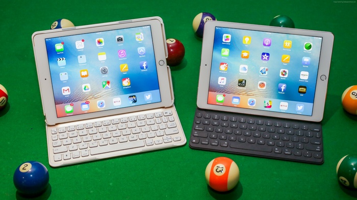Two iPads with keyboards on a pool table with billiard balls
