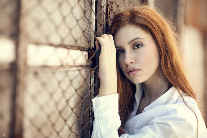 Redhead woman leaning against a fence