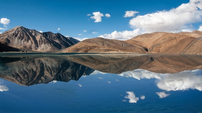 Mountain range reflected in a calm lake under a blue sky with clouds