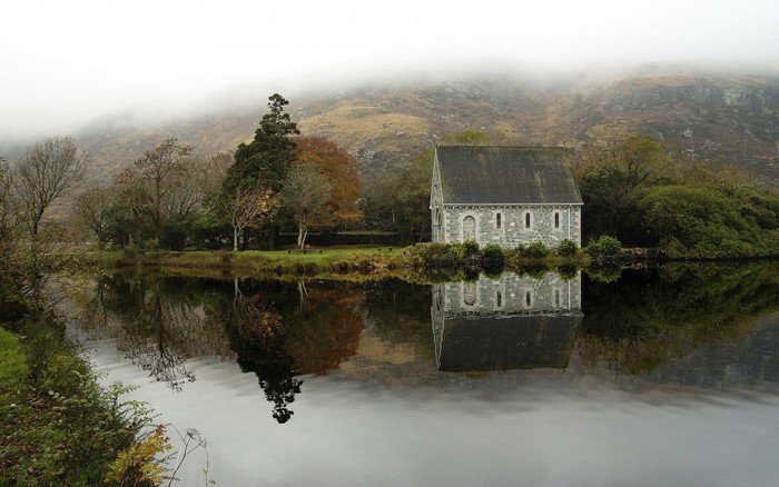 Stone chapel reflected in a misty lake with hills