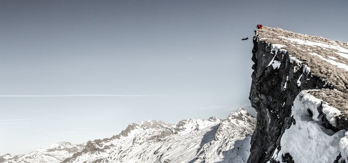 Man in wingsuit jumps off a snowy mountain cliff