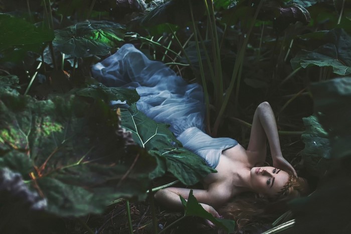 Woman in a blue dress lying in a forest