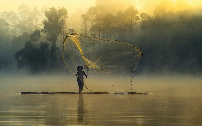 Fisherman casting net on misty lake at sunrise