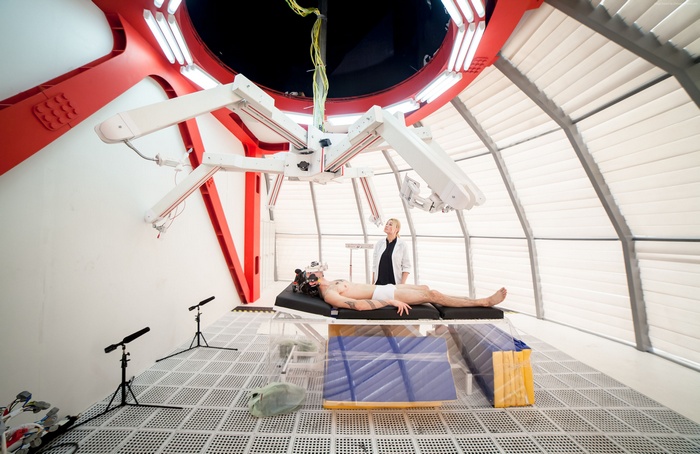 Man on medical bed with VR headset and robotic arms