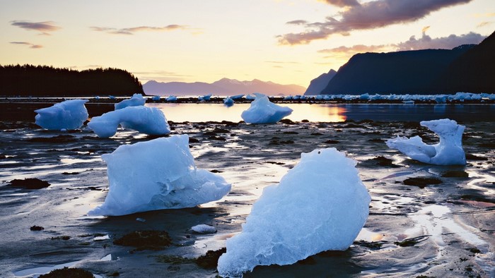 Icebergs on a beach at sunrise with mountains in the background