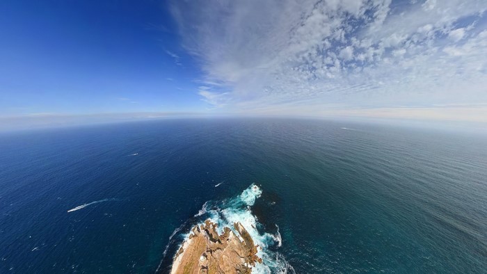 Ocean waves crashing on a rocky cape under a blue sky