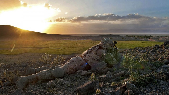 Soldier aiming rifle on a hill at sunset