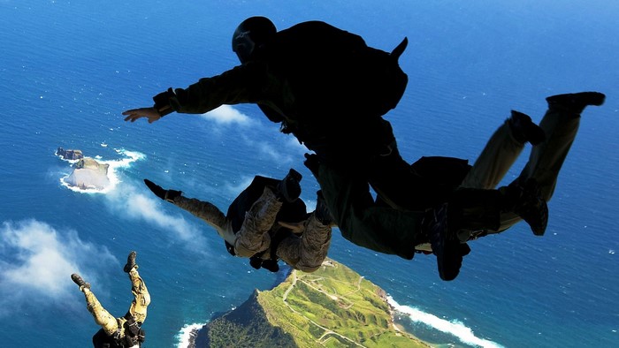 Paratroopers skydiving over a coastal landscape