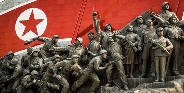 Statue of soldiers in front of North Korean flag