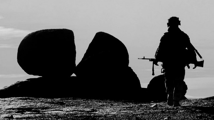 Soldier with rifle walking past rocks in monochrome